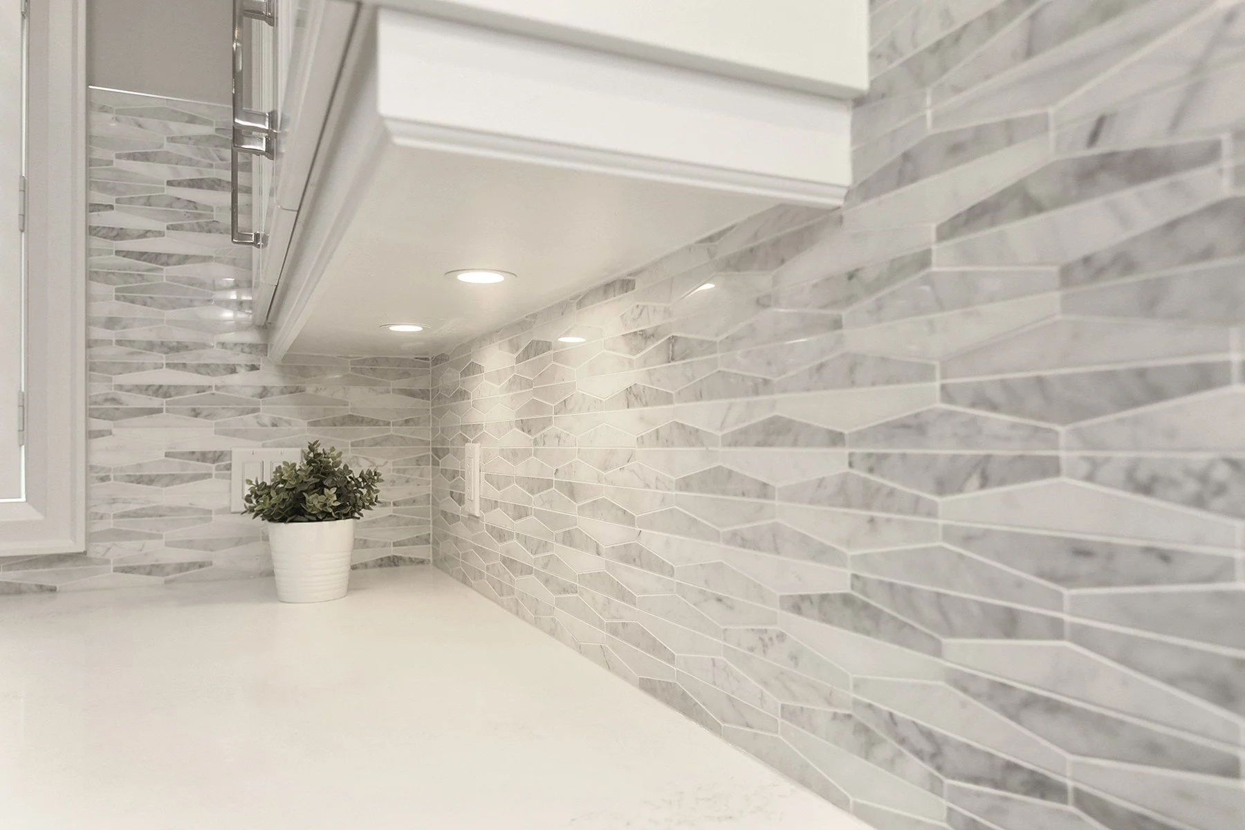 White kitchen counter with grey mosaic backsplash and under-cabinet lighting in a clean, finished detail shot.