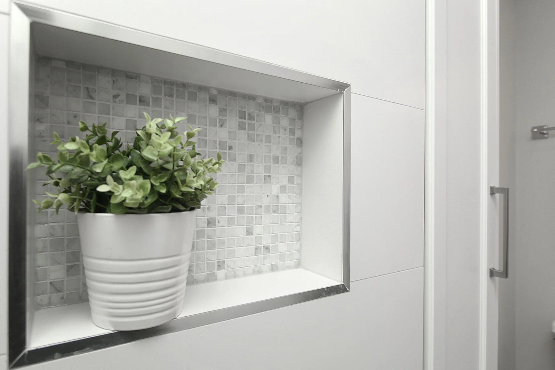 Bright shower niche with mosaic tile, white wall tile, and a small potted plant in a clean bathroom.