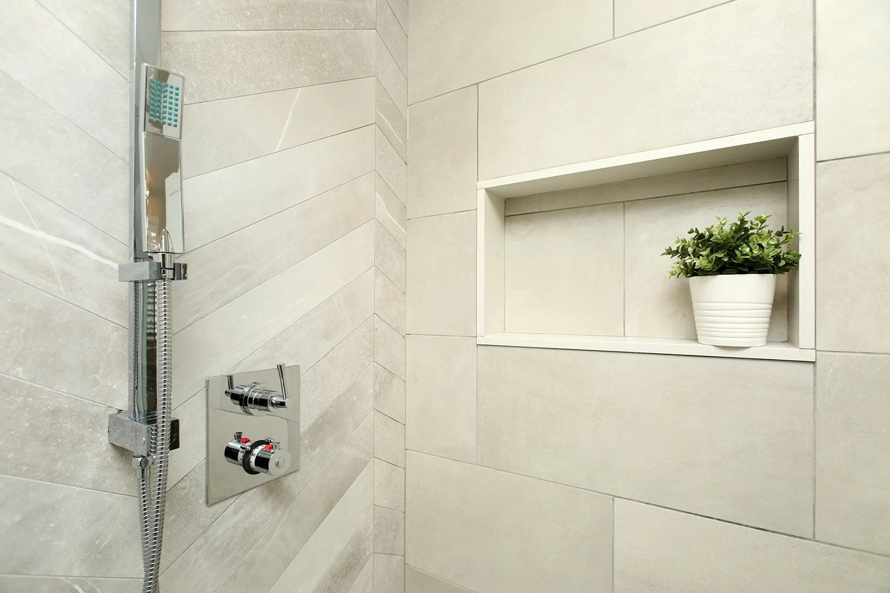 Warm white shower with large-format tile, chrome fixtures, and a recessed niche with a small potted plant.