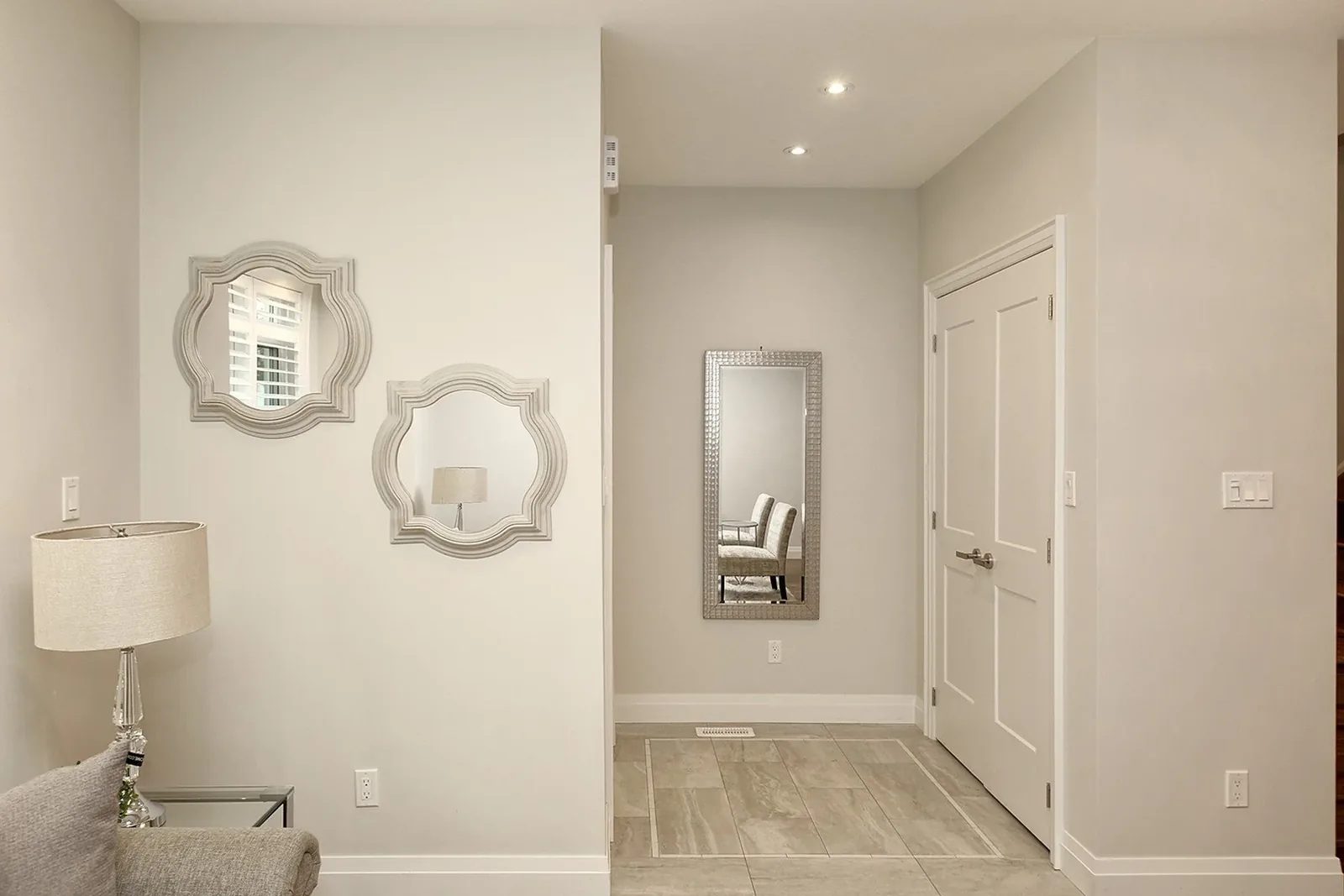Bright entry hall with greige walls, white trim, large floor tile, recessed lights, and staged mirrors.