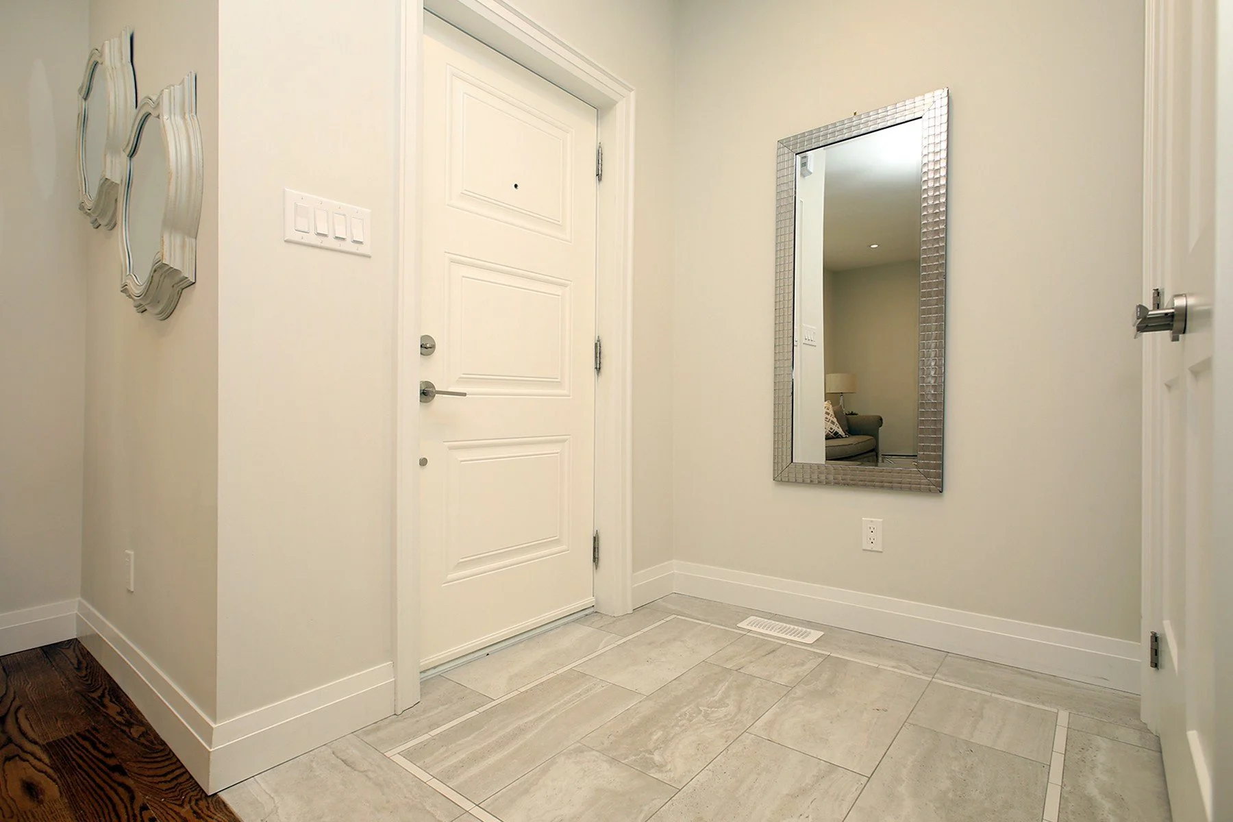 Bright condo entry with a large mirror, pale tile flooring, white trim, and dark hardwood beyond.