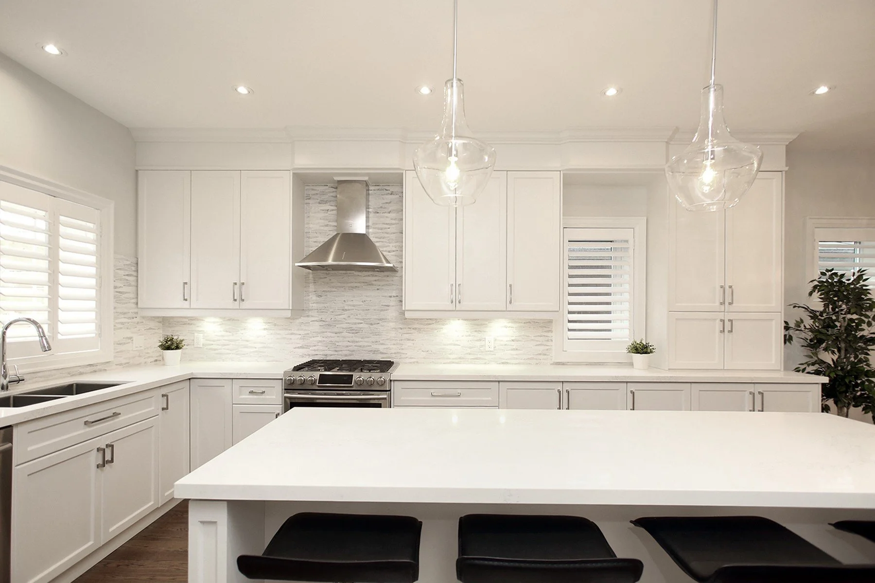Bright white kitchen renovation with a large quartz island, shaker cabinets and glass pendants.