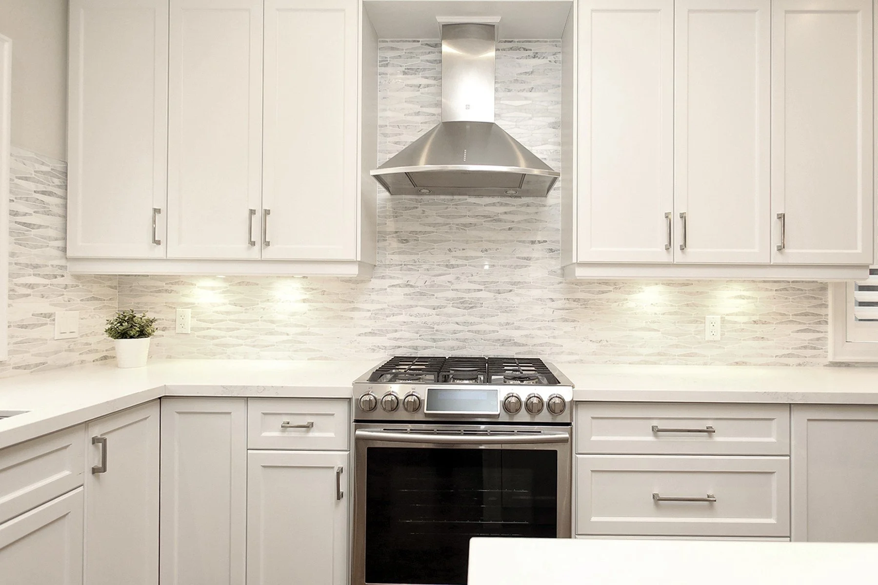 Warm white kitchen with shaker cabinets, quartz counters, mosaic tile backsplash and a centred steel range hood.