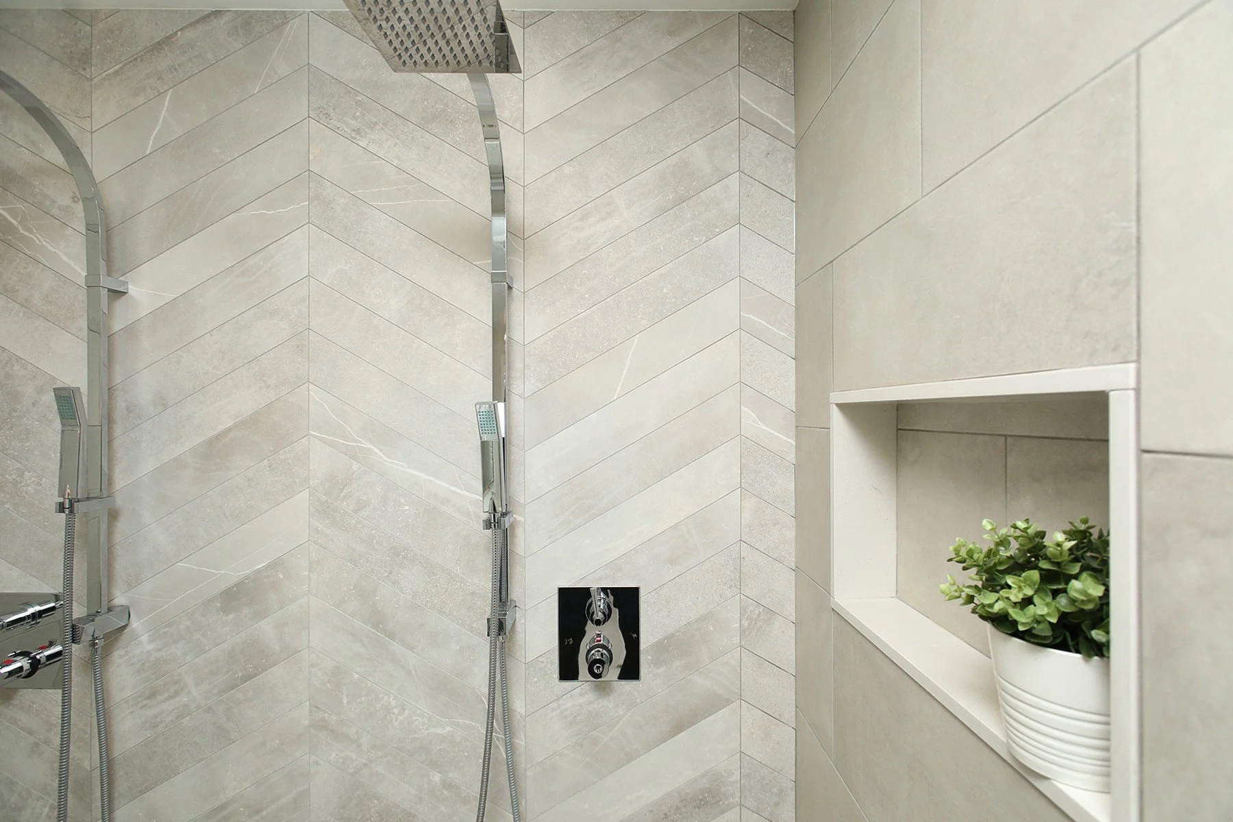 Bright shower renovation with light greige tile, chrome fixtures, and a recessed niche with greenery.