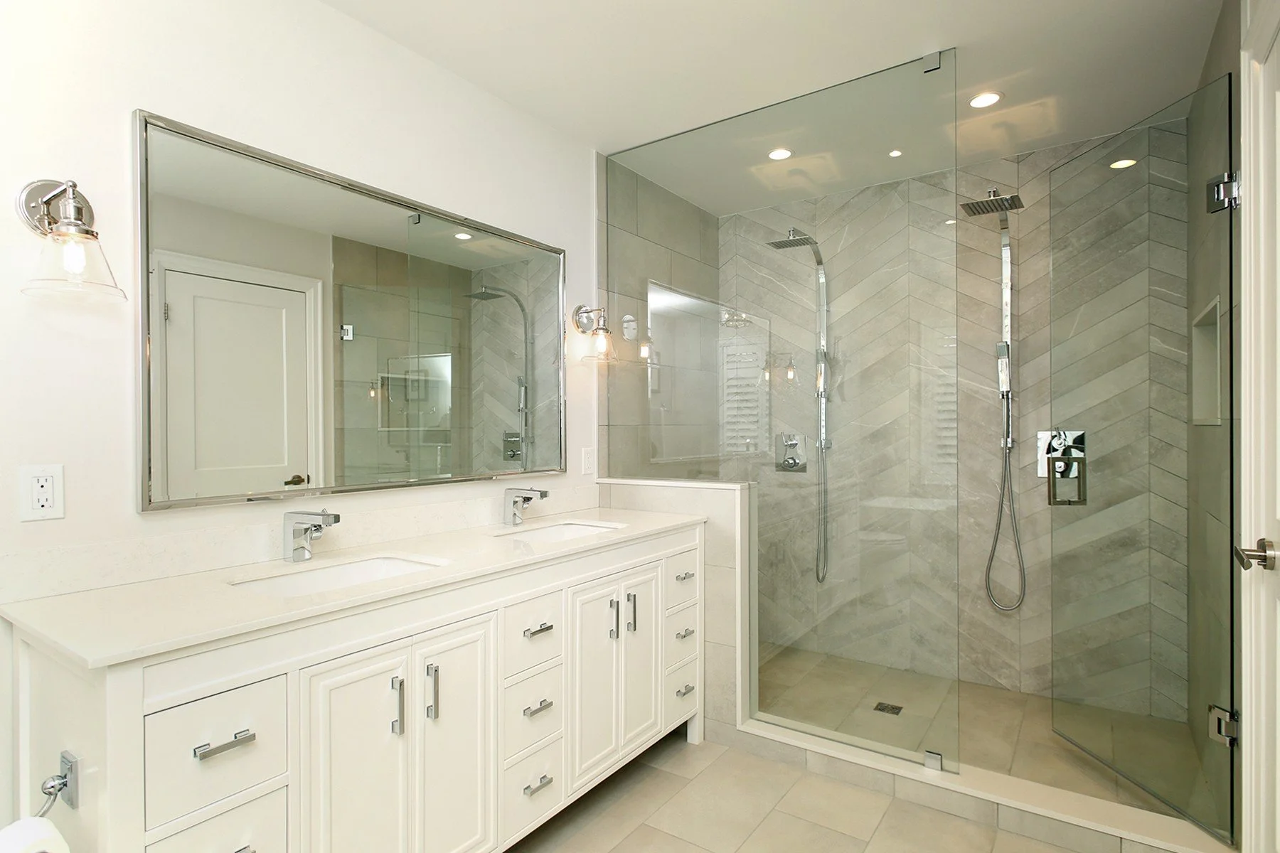 Bright white bathroom with a double vanity, framed mirror, and glass walk in shower with light grey tile.