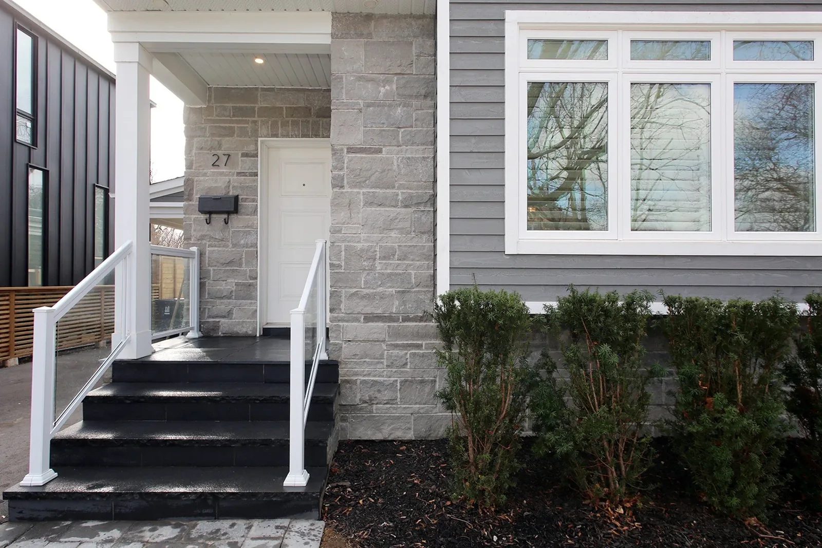 Finished front entry with grey stone, white railings, black steps and a large front window.