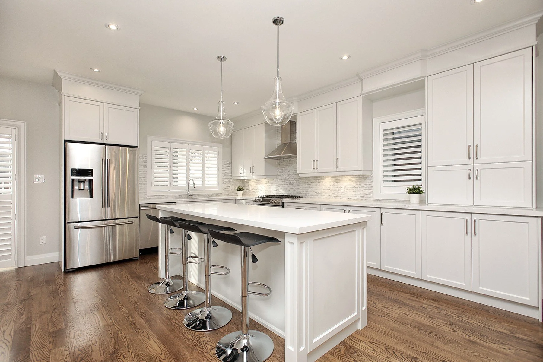 Bright white kitchen with shaker cabinetry, a large quartz island, glass pendants, and warm wood floors.