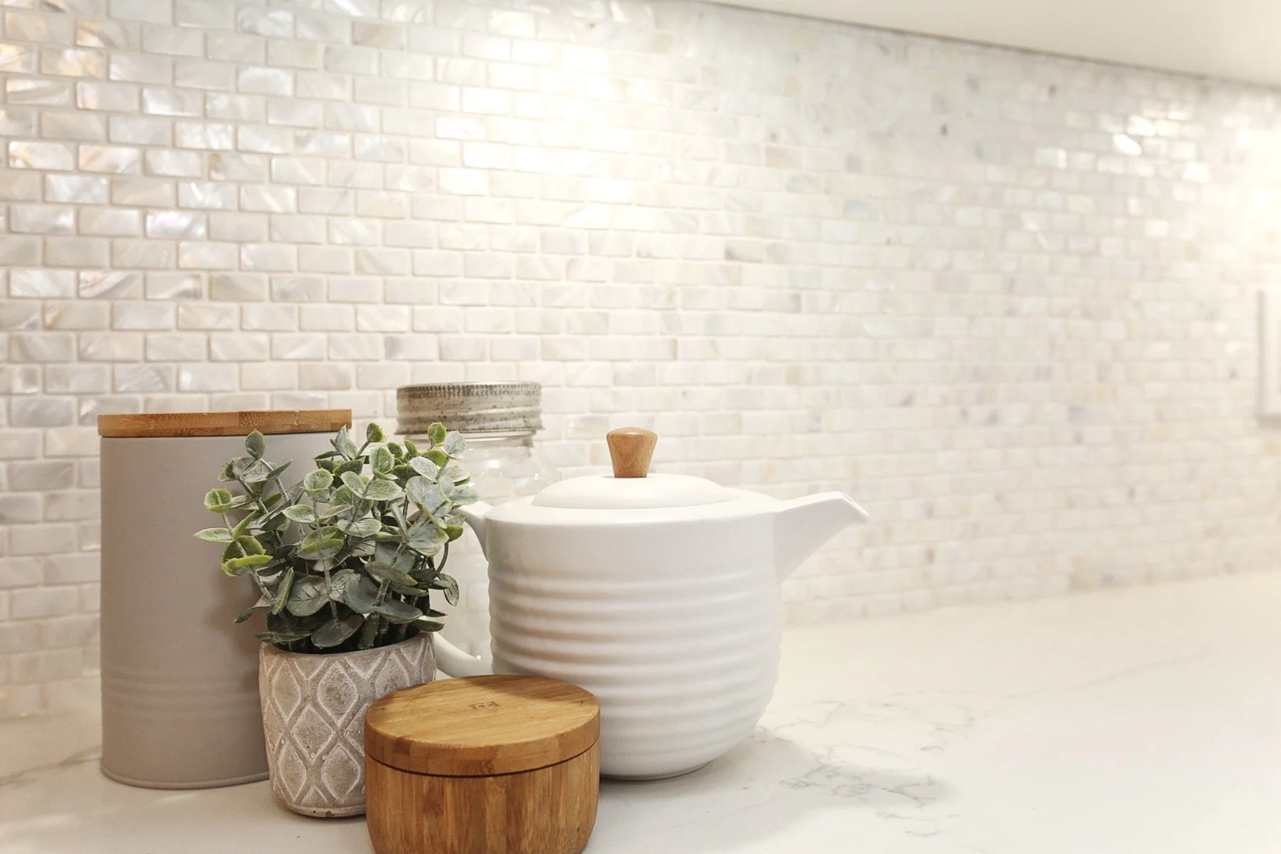 Warm white kitchen backsplash detail with glossy tile, pale stone counter, and natural wood accents.