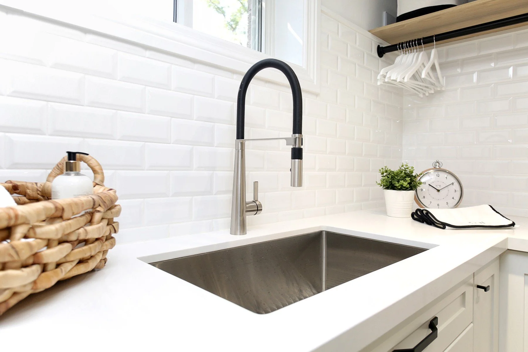 Bright laundry room detail with white tile, quartz counter, black faucet, and hanging rail above the sink.