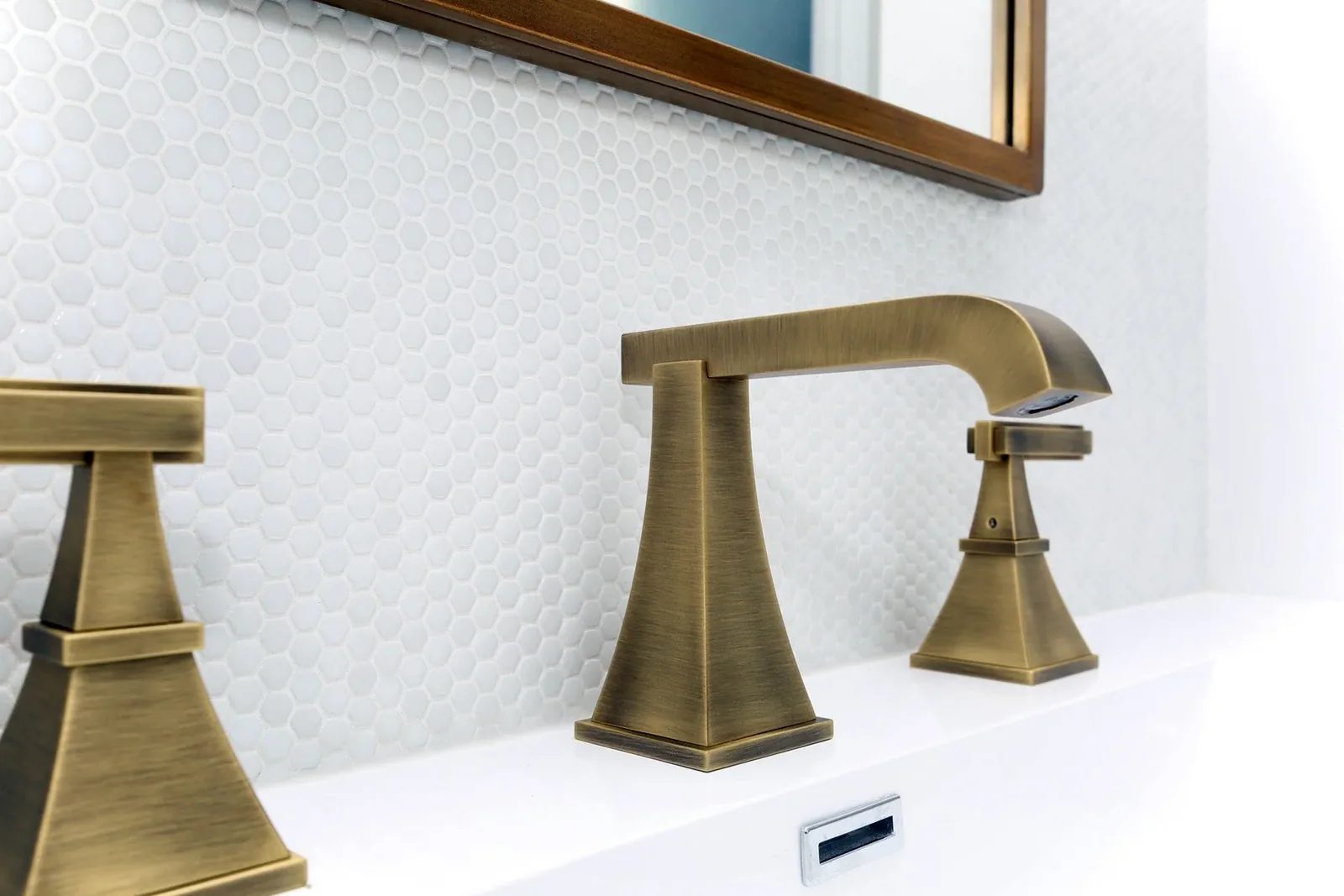 Brushed brass bathroom faucet set against white hex tile and a clean vanity in a polished renovation detail.