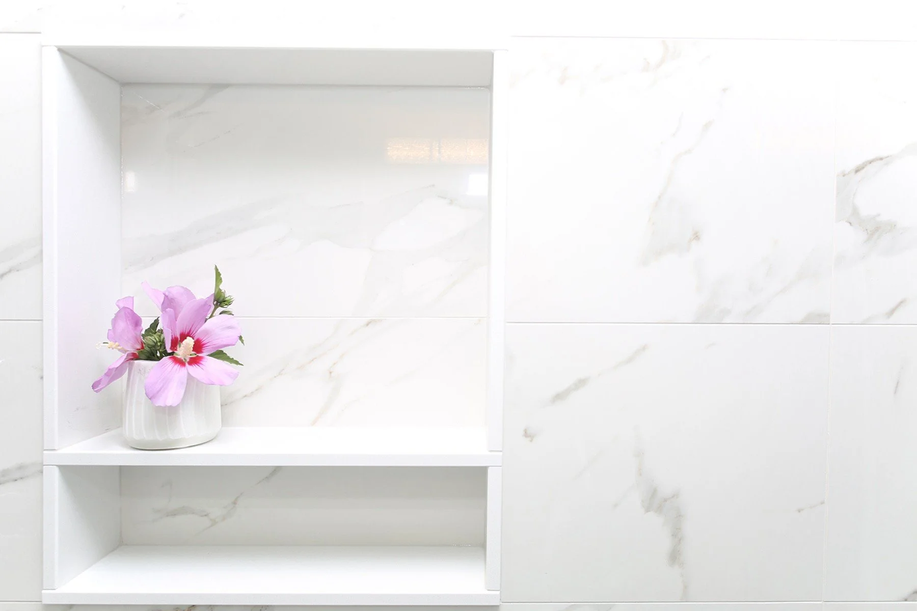 White recessed bathroom niche with marble-look tile and pink flowers, styled as a clean renovation detail.