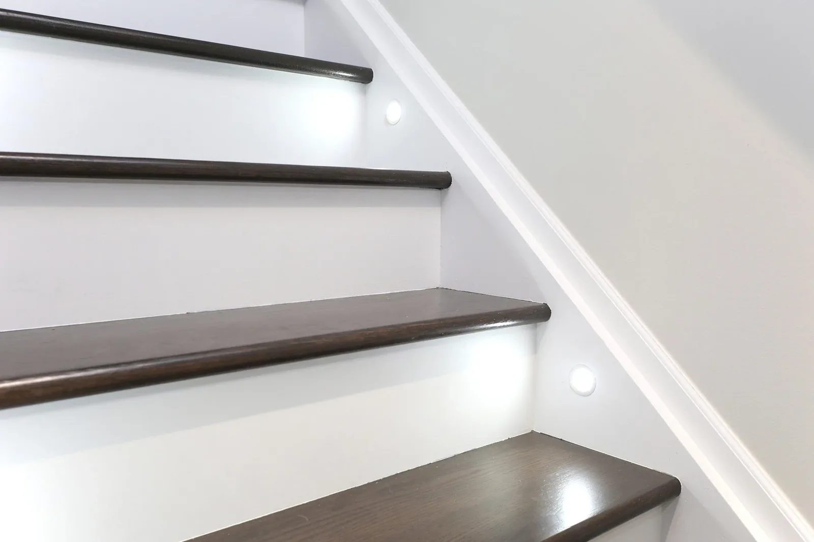 Dark stained wood stair treads with white risers and recessed wall lights in a clean finished stairway.