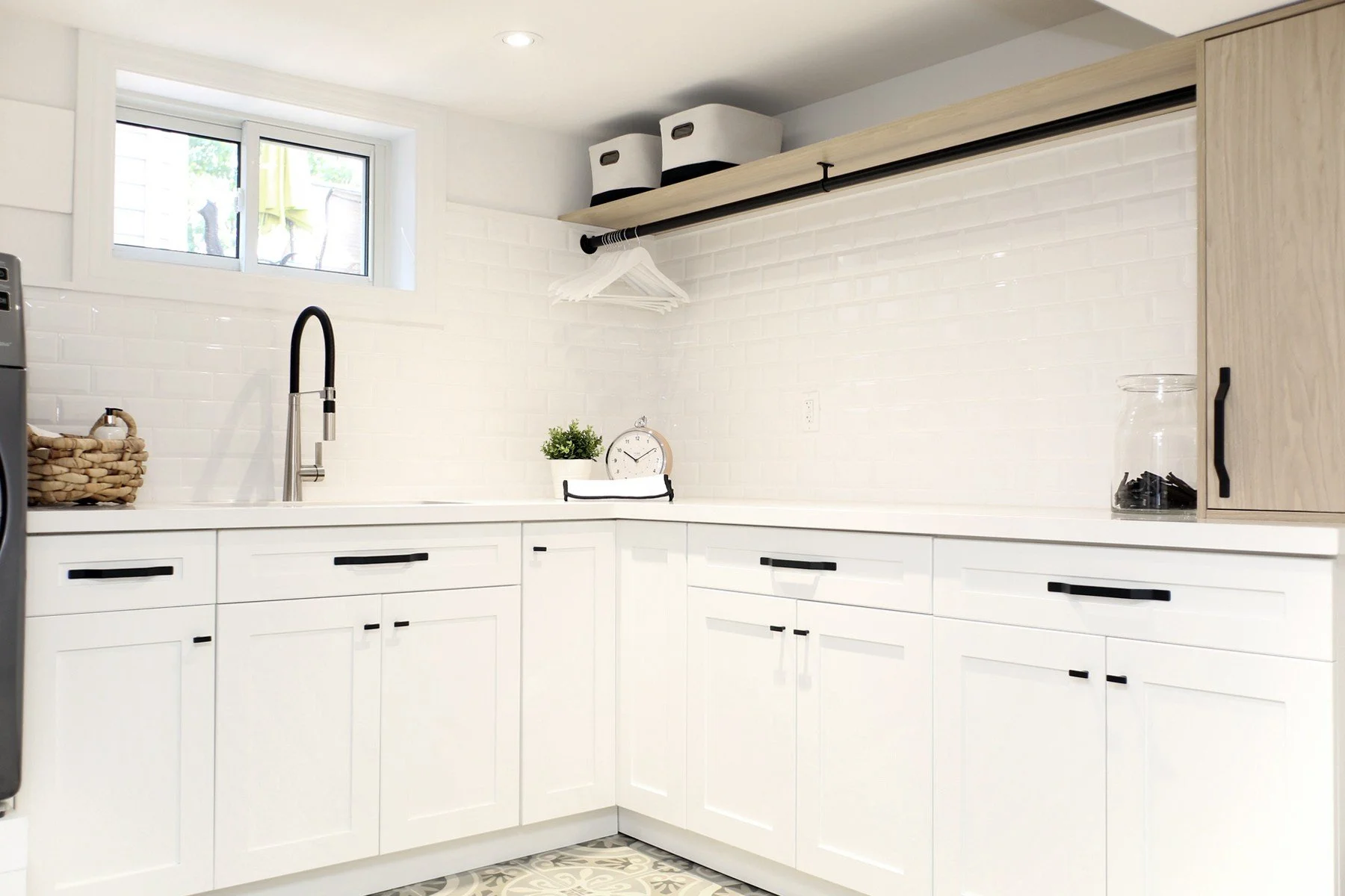 Bright laundry room with white shaker cabinets, black hardware, a wall drying rail and glossy tile.