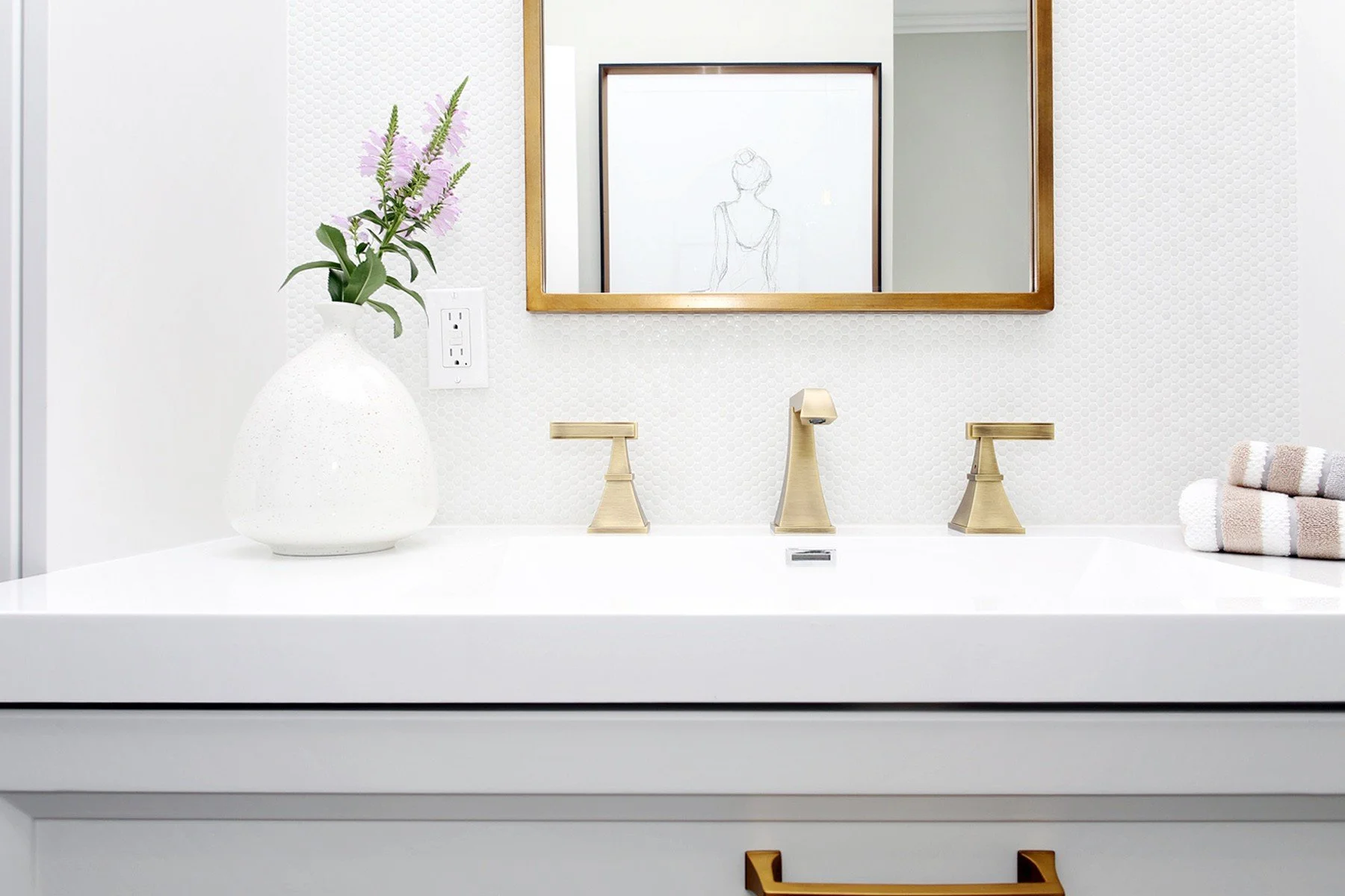 Soft white bathroom vanity with brass fixtures, a framed mirror, and neatly organised folded towels.