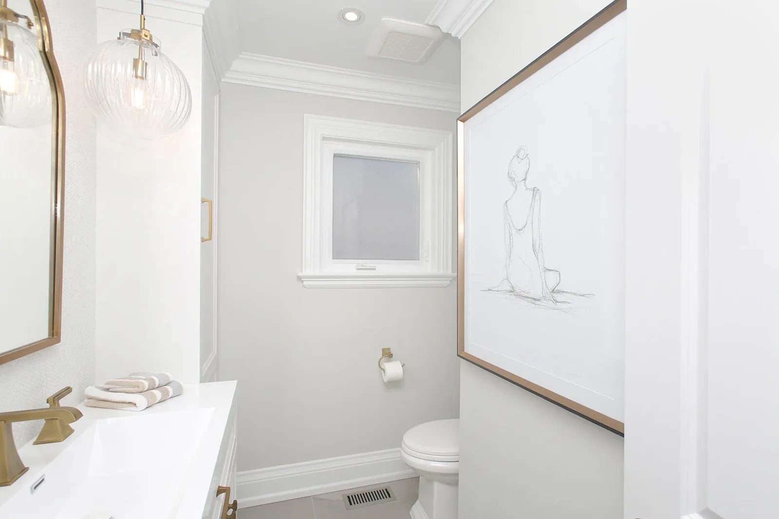 Bright powder room with white vanity, brass fixtures, grey walls, framed art, and classic trim.