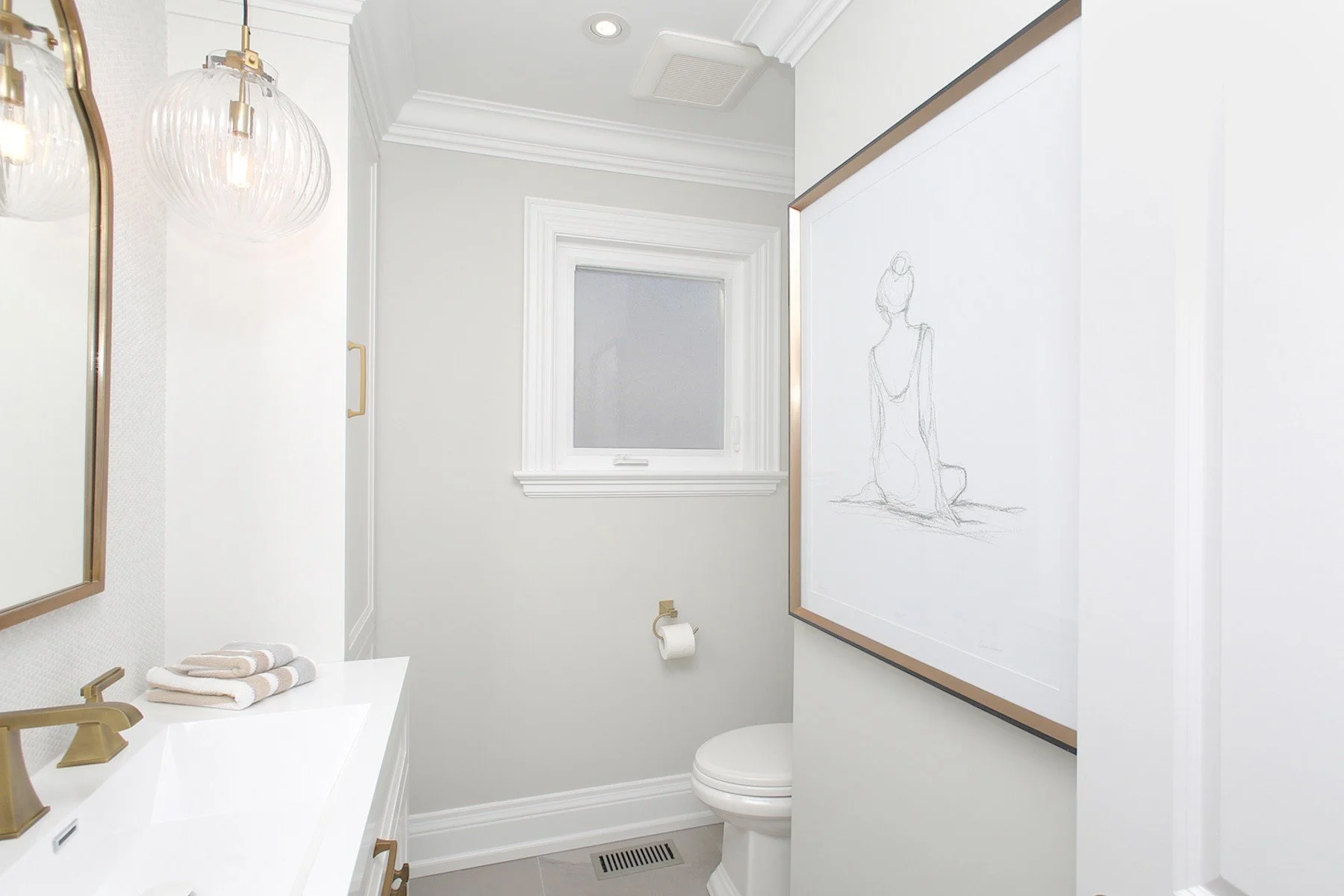 Bright powder room with white vanity, brass fixtures, grey walls, framed art, and classic trim.