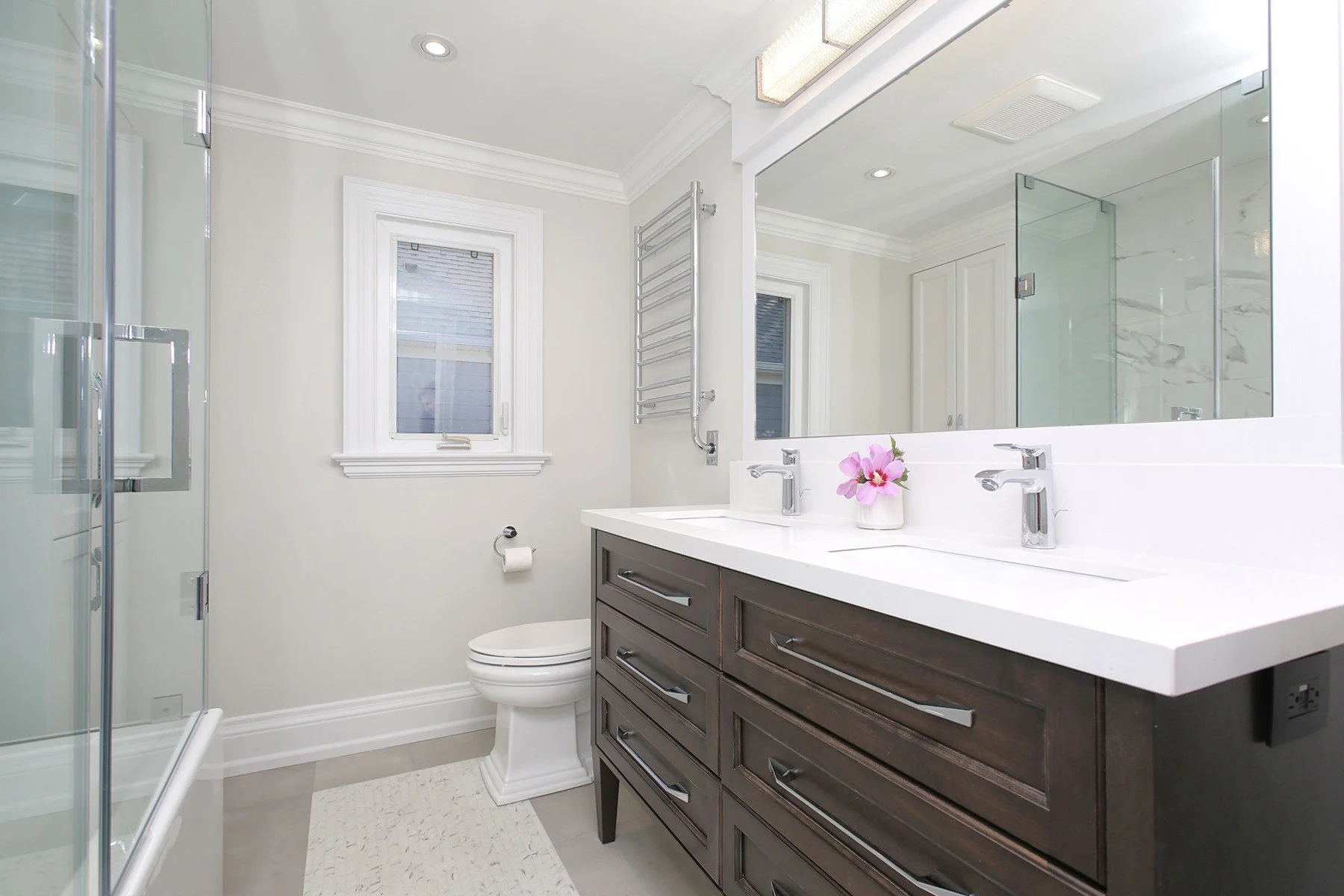 Bright renovated bathroom with a dark wood double vanity, glass shower, white walls and chrome fixtures.