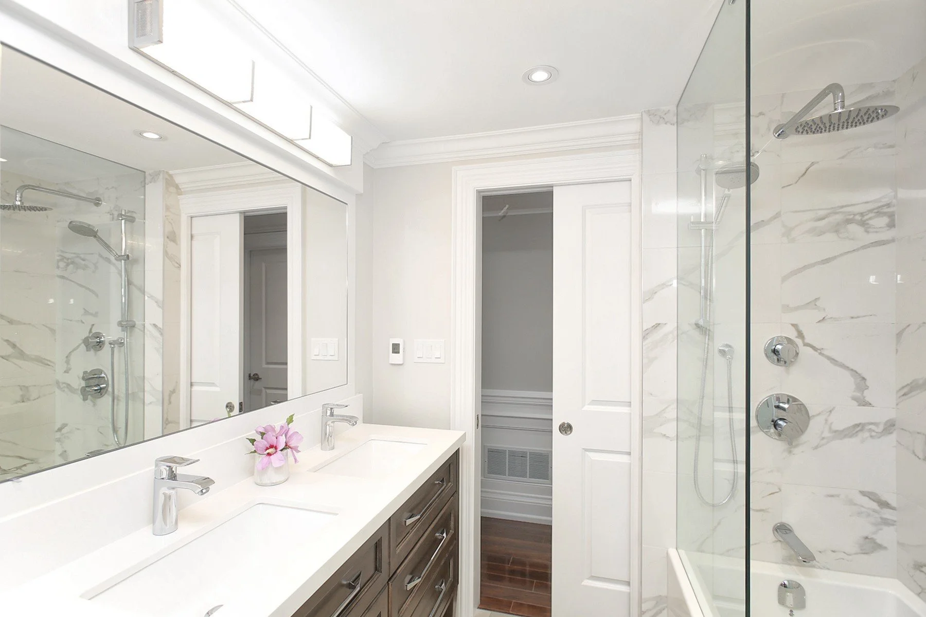 Bright renovated bathroom with a double vanity, marble style shower walls, and chrome fixtures.
