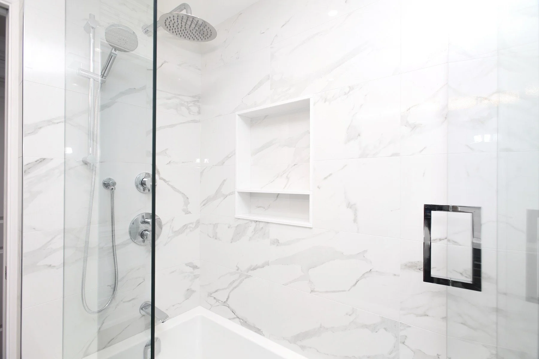 Bright white marble look shower with a glass enclosure, tub base and recessed wall niche.