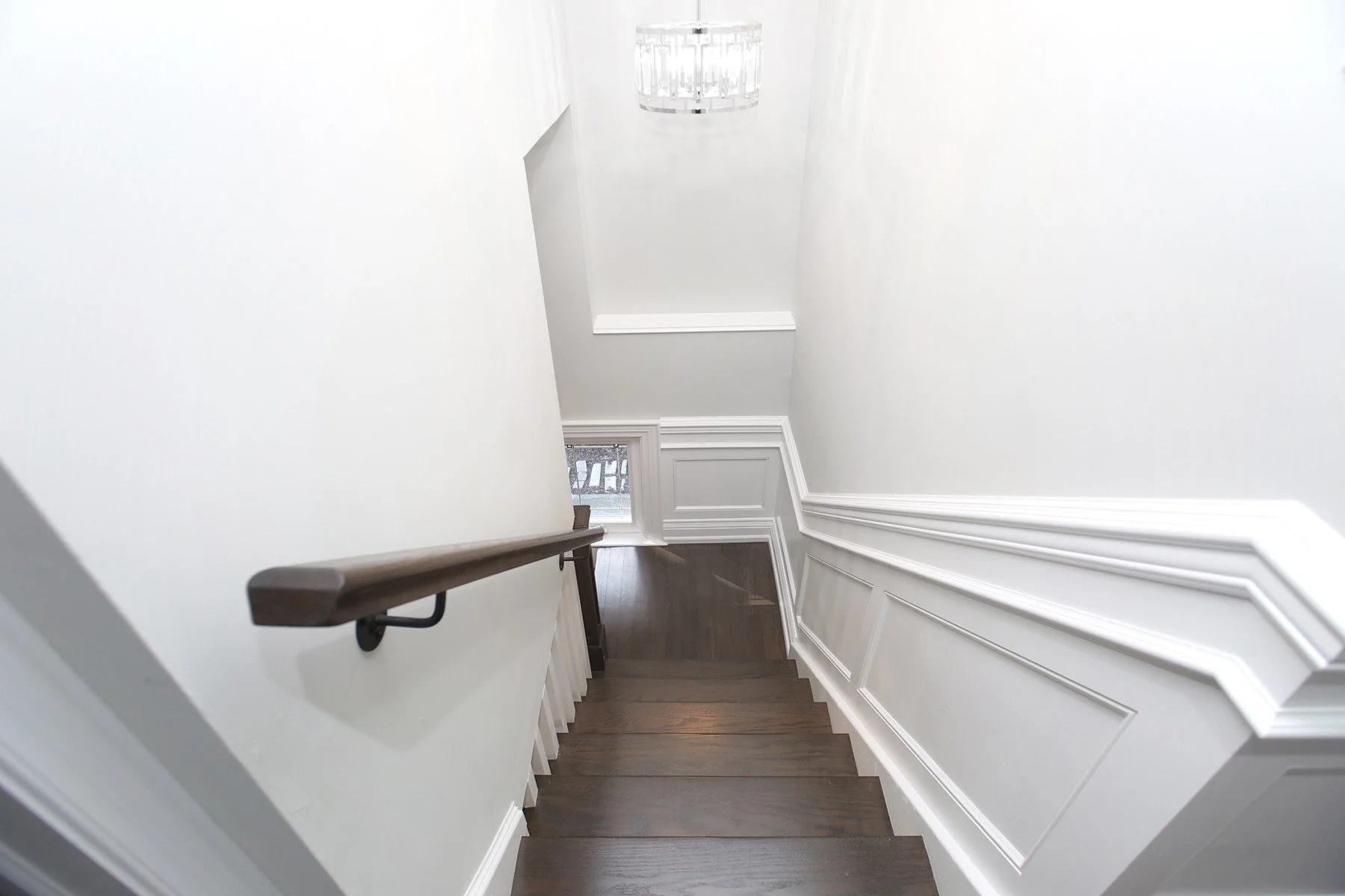 Bright white stair hall with dark wood treads, classic wall panelling, and a modern ceiling light.