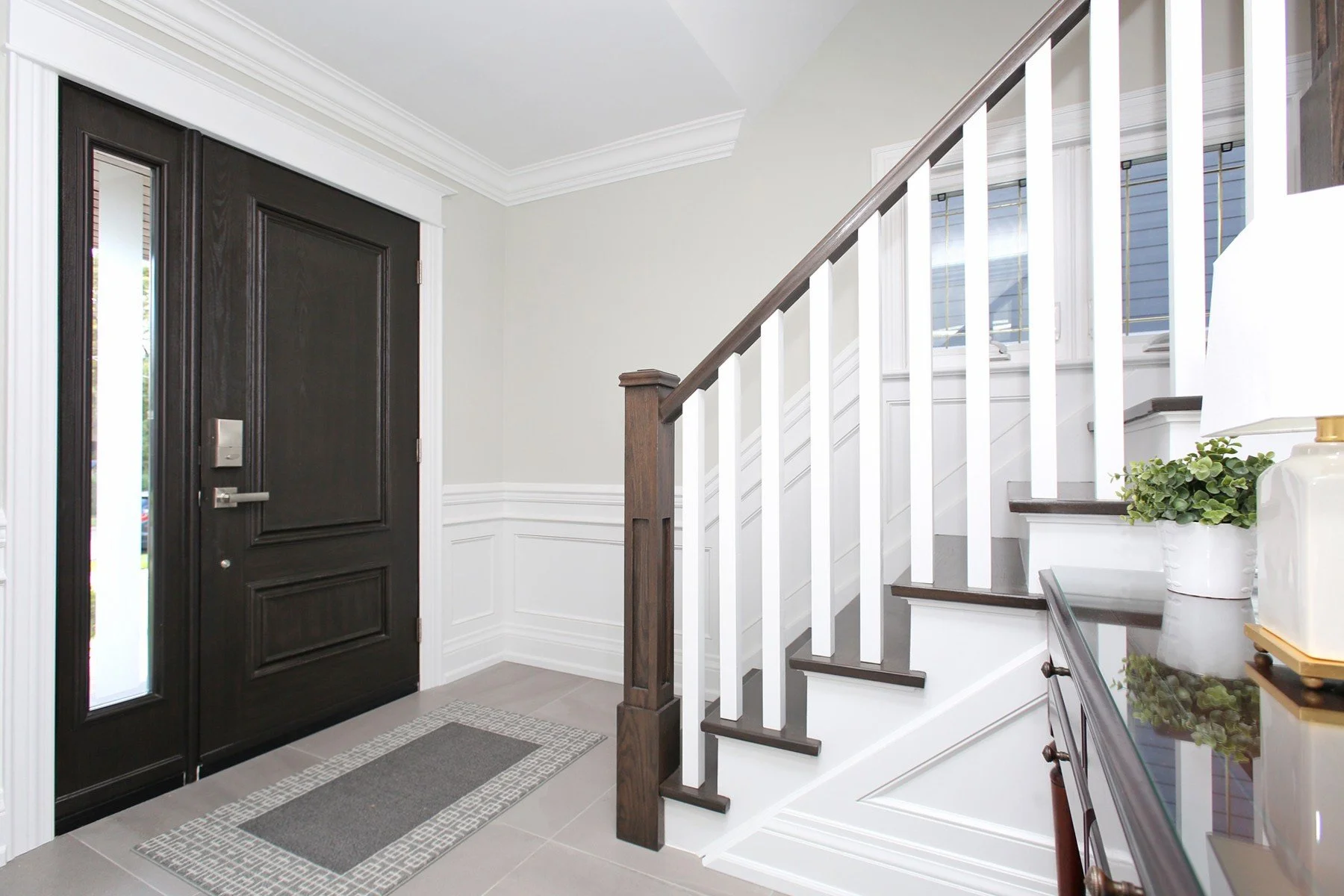 Bright transitional entry with dark wood front door, white millwork, and staircase with contrasting treads.