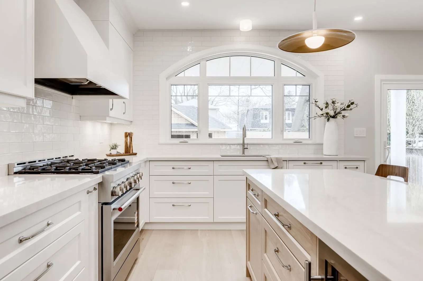 Coastal Blue: charcoal grey arched built-in shelving flanking the living room fireplace, seen across the quartz-topped kitchen island, by Waterfront Home Improvements