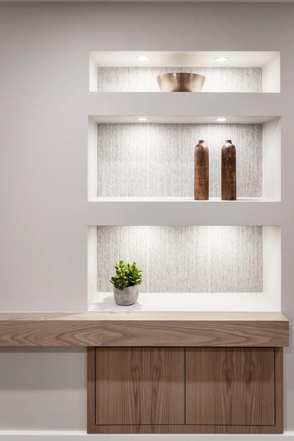 Lit wall niches above a wood cabinet create a calm modern hallway feature with soft white and wood tones.