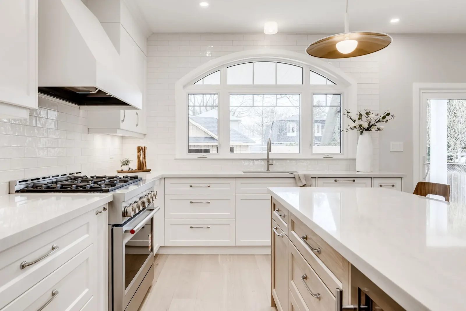 Range wall with the stainless range under a custom white hood, a glazed subway backsplash and the arched window over the sink, with the oak island in the foreground.
