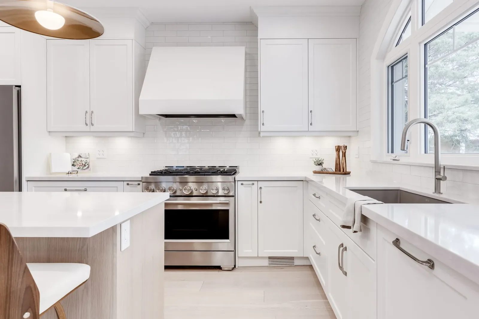 Corner of the kitchen with the white hood over the stainless range, the sink run under the window and the island edge in the foreground.