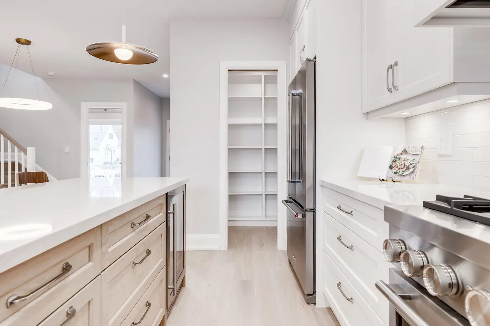 Island run toward the walk-in pantry standing open beyond the fridge, with full-height white shelving inside.