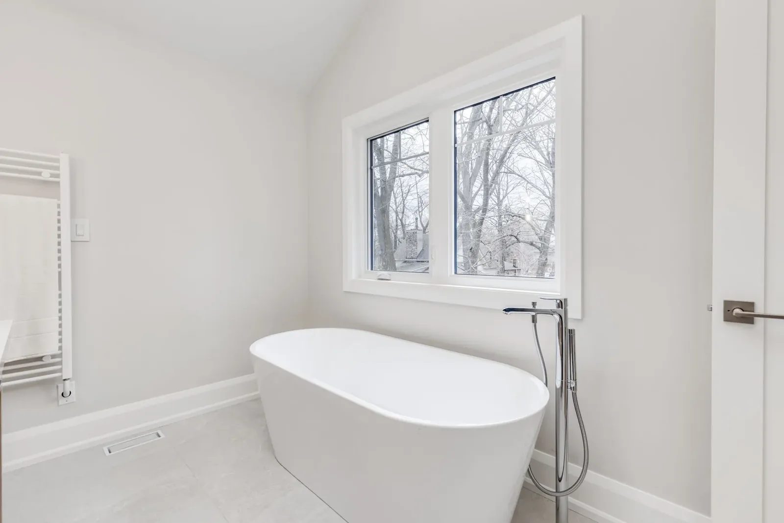 Freestanding oval tub beneath the vaulted ensuite windows, with a chrome floor-mounted filler beside it.