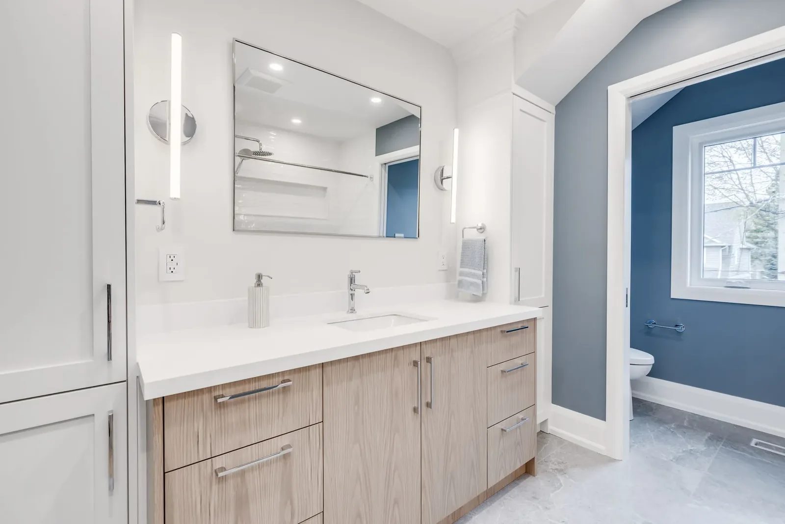 Main bathroom with a textured light oak vanity and tall linen cabinet, and the arched opening through to the blue accent room beyond.