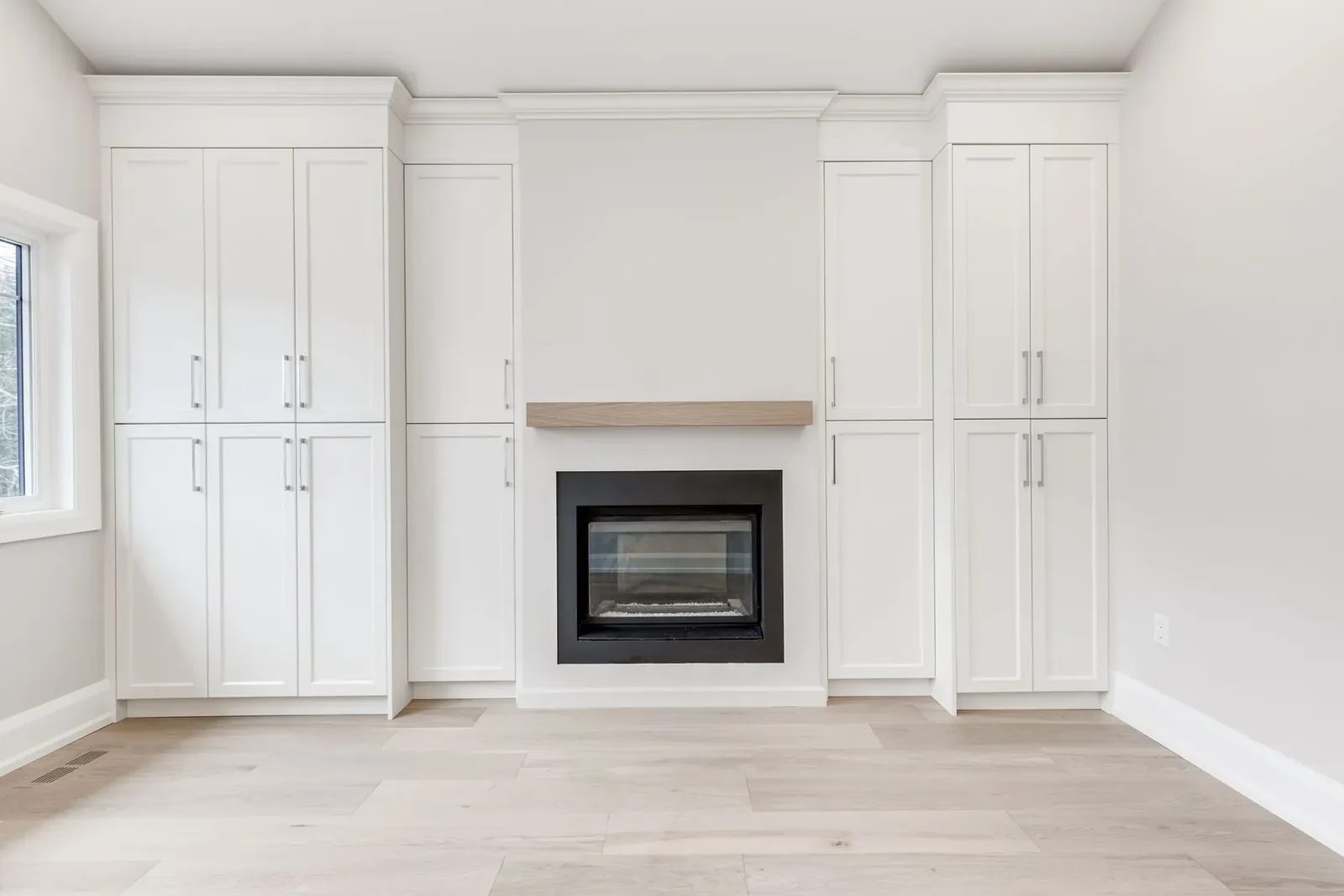 Primary bedroom fireplace wall, with tall white built-in wardrobes flanking the fireplace under its oak mantel shelf.