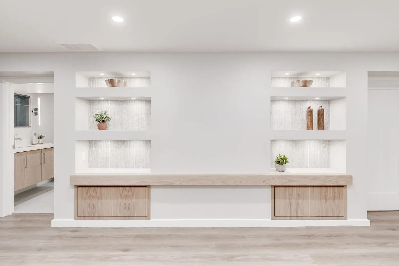 Basement feature wall straight on, twin stacks of lit niches over the floating oak bench, with the bathroom beyond the doorway.