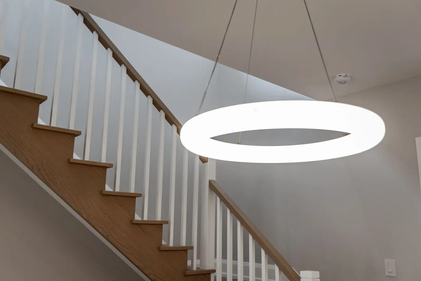 Oak stair treads and white spindles under an oak handrail, with a lit ring pendant hanging in the stairwell.