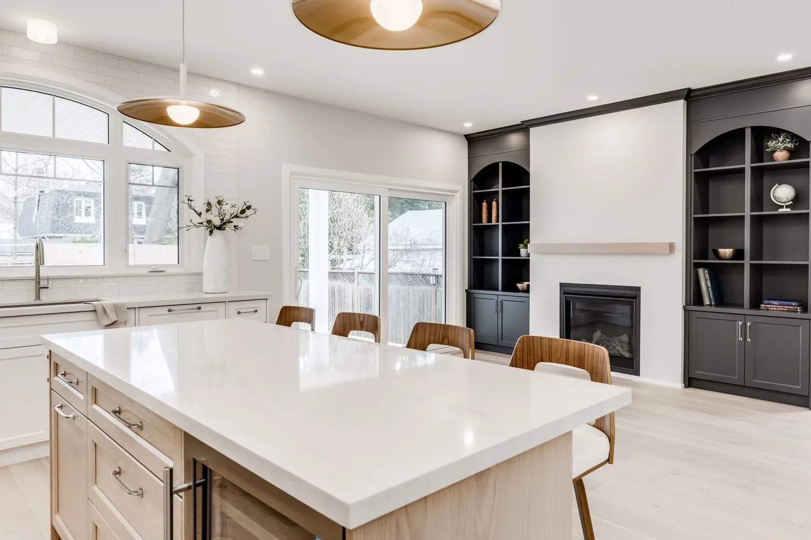 View across the quartz-topped kitchen island to charcoal grey arched built-in shelving flanking the living room fireplace.