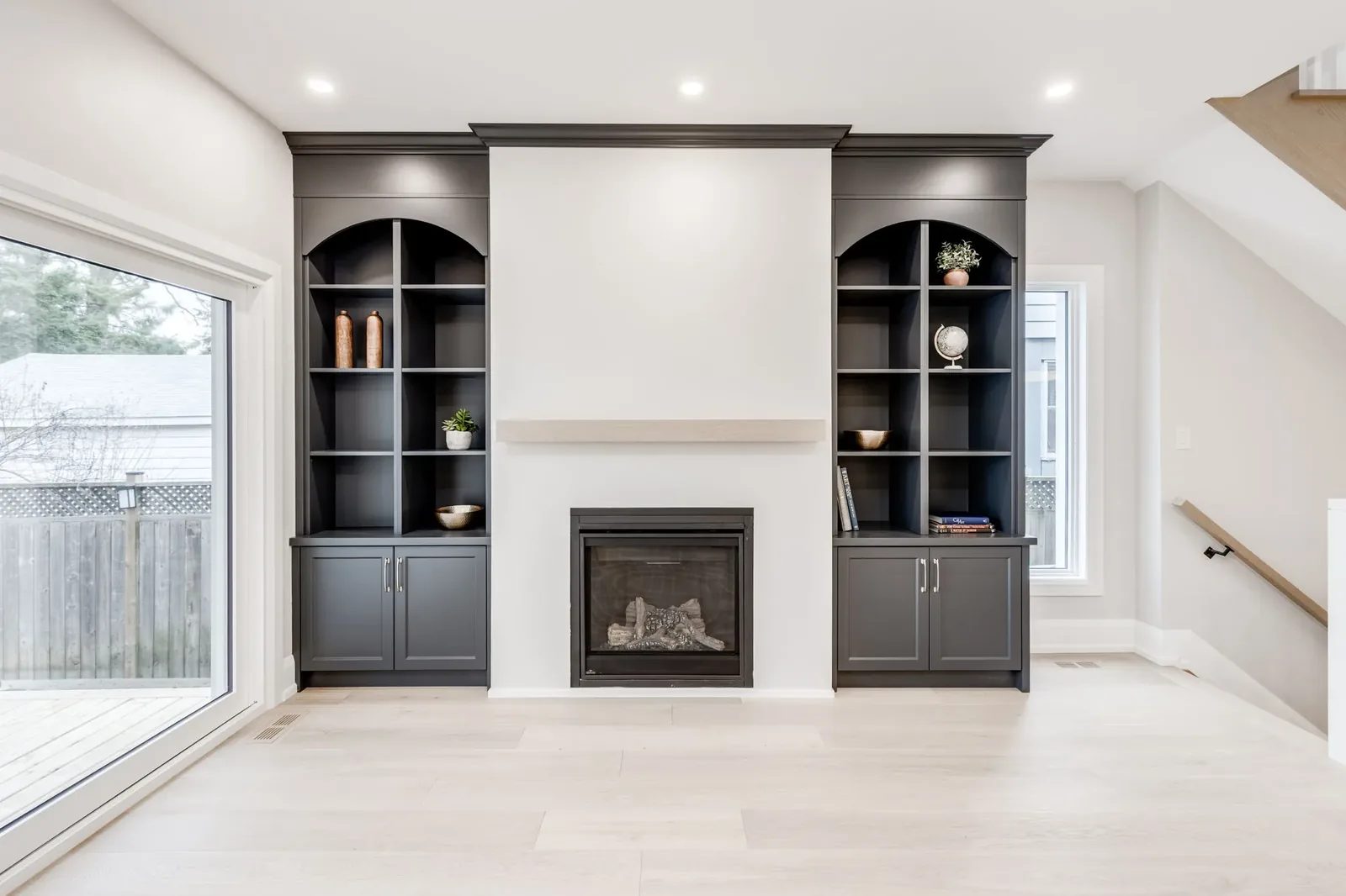 A newly renovated living room with custom charcoal grey built-in shelving flanking a modern fireplace with a light wood mantle.