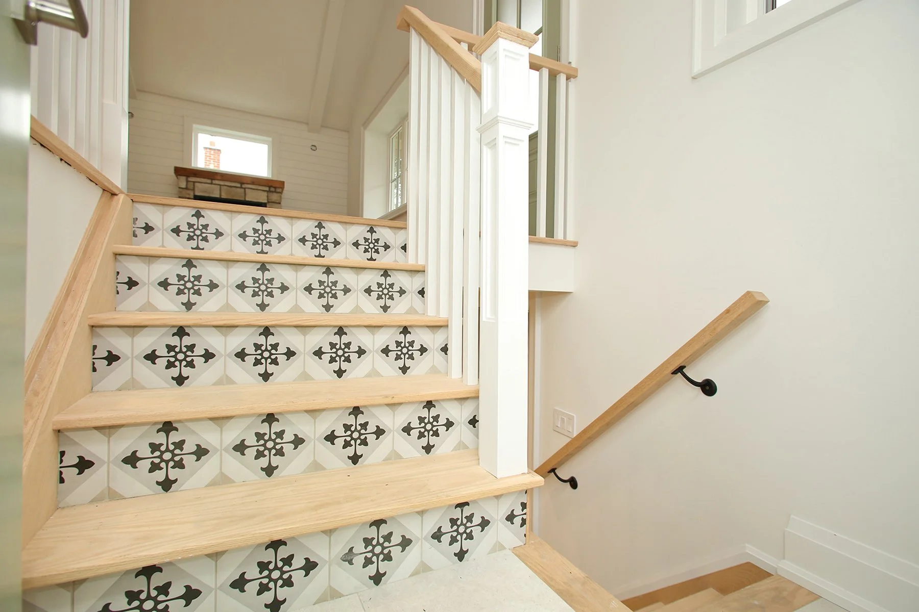 Oak stair treads with black and white patterned tile risers rising past white spindles to a bright upper landing.