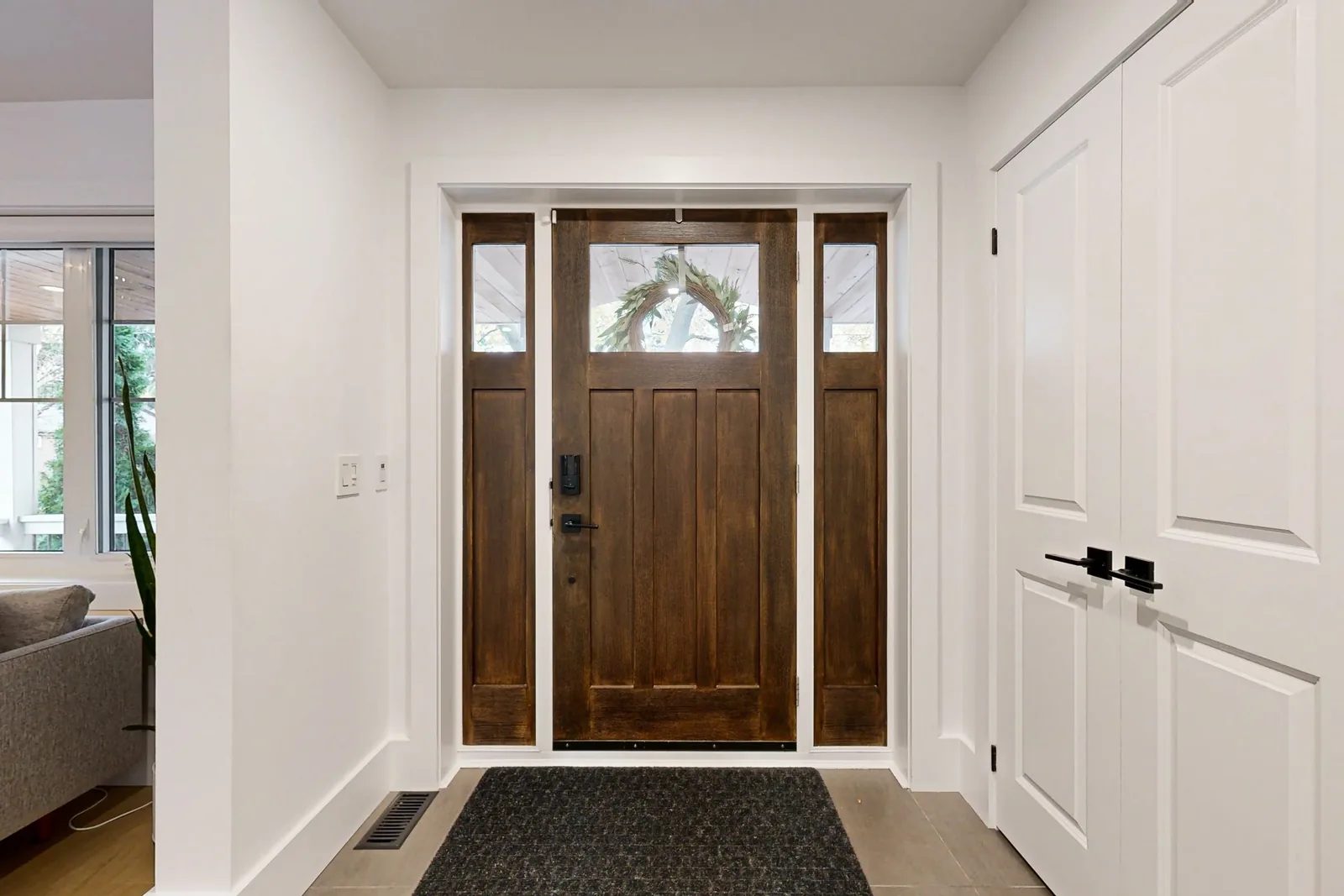 Bright front entry with a stained wood door, narrow sidelights, white walls, and black hardware.