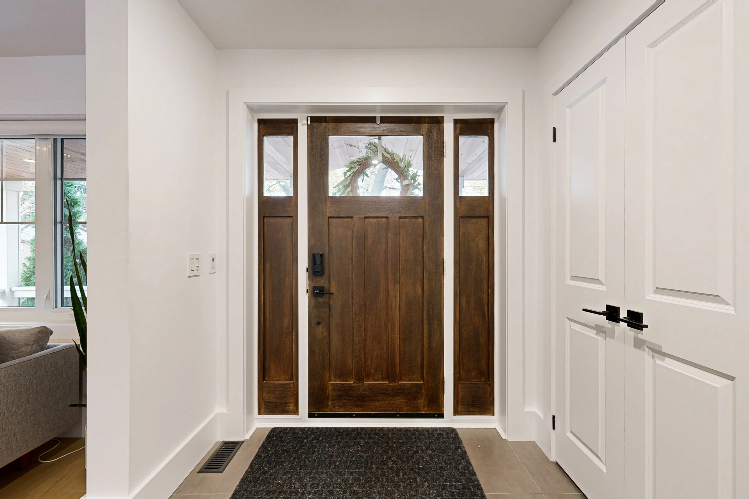Bright front entry with a stained wood door, narrow sidelights, white walls, and black hardware.
