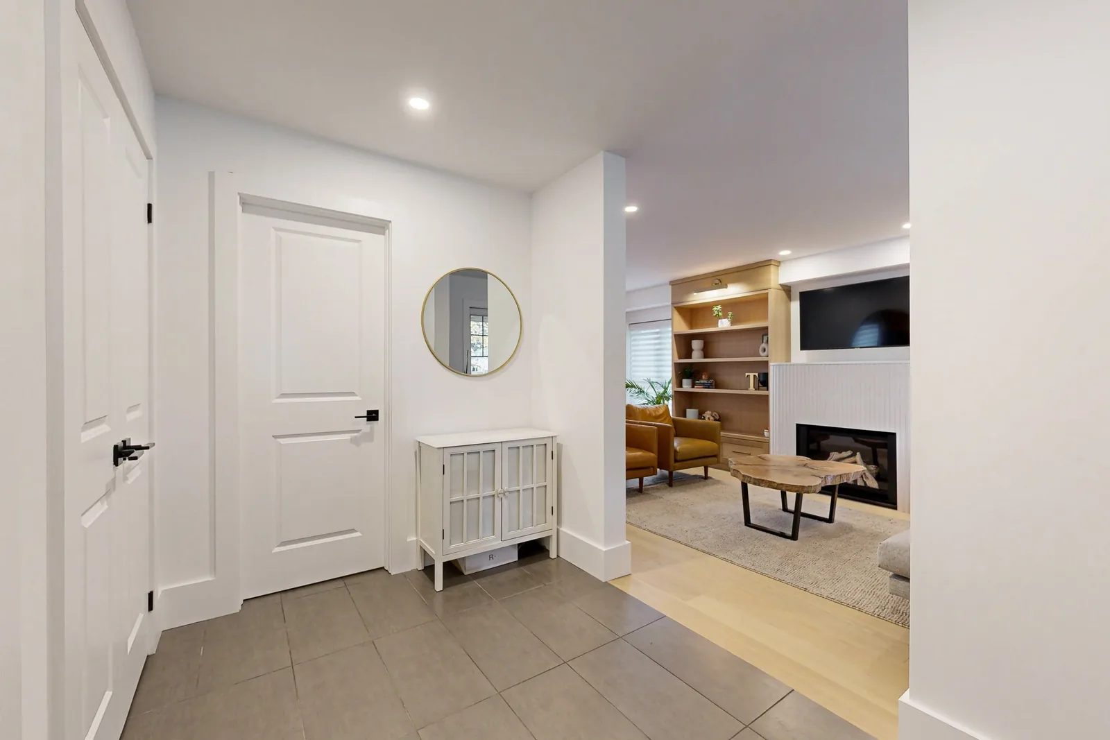 Bright finished entry with grey tile, white doors, and a view into a warm living room with built-in shelving.