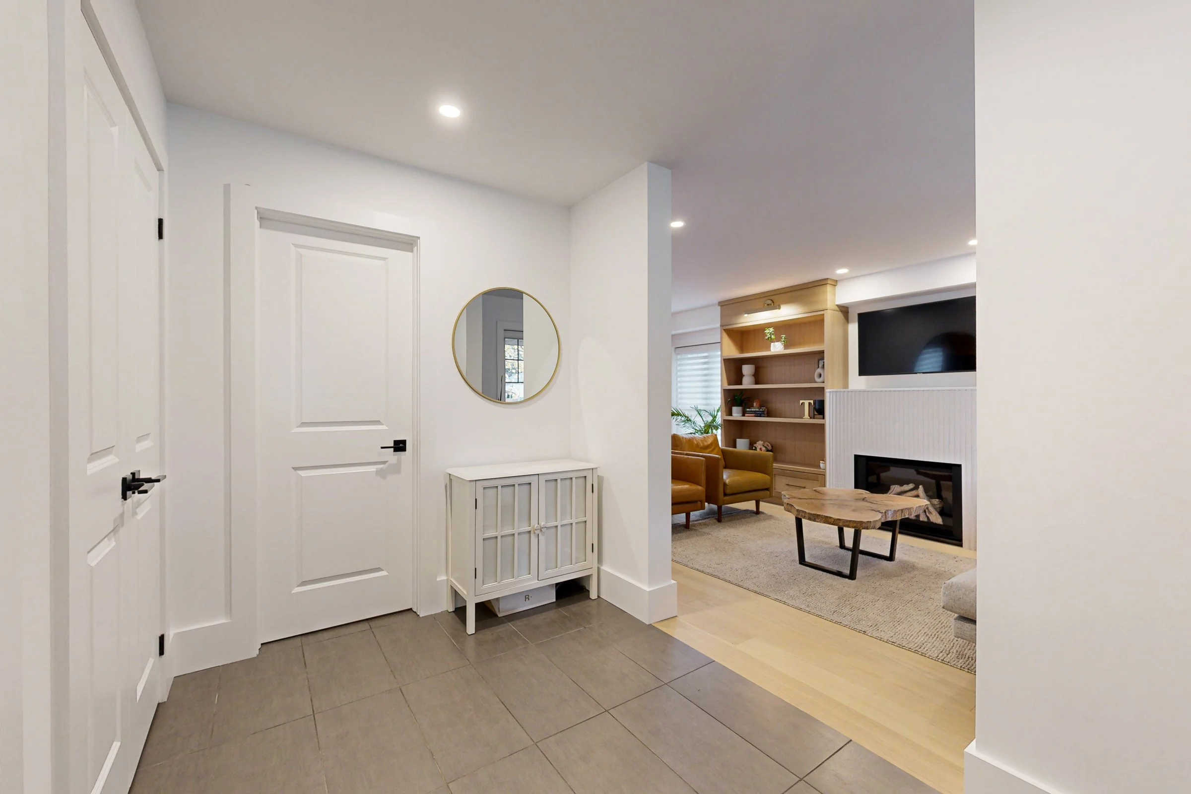 Bright finished entry with grey tile, white doors, and a view into a warm living room with built-in shelving.