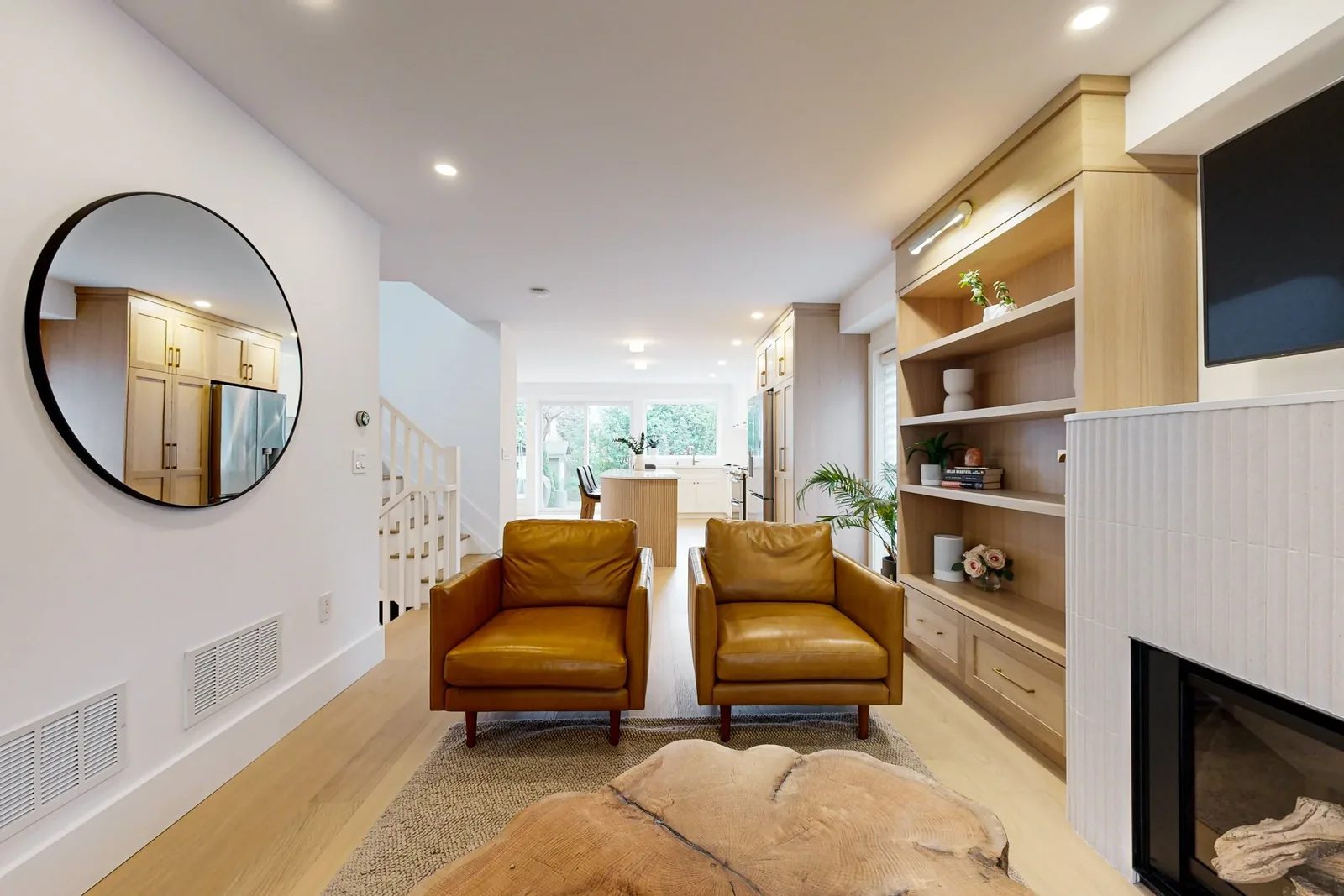 Bright open living area with oak built-ins, leather chairs, a tiled fireplace, and kitchen sightlines.