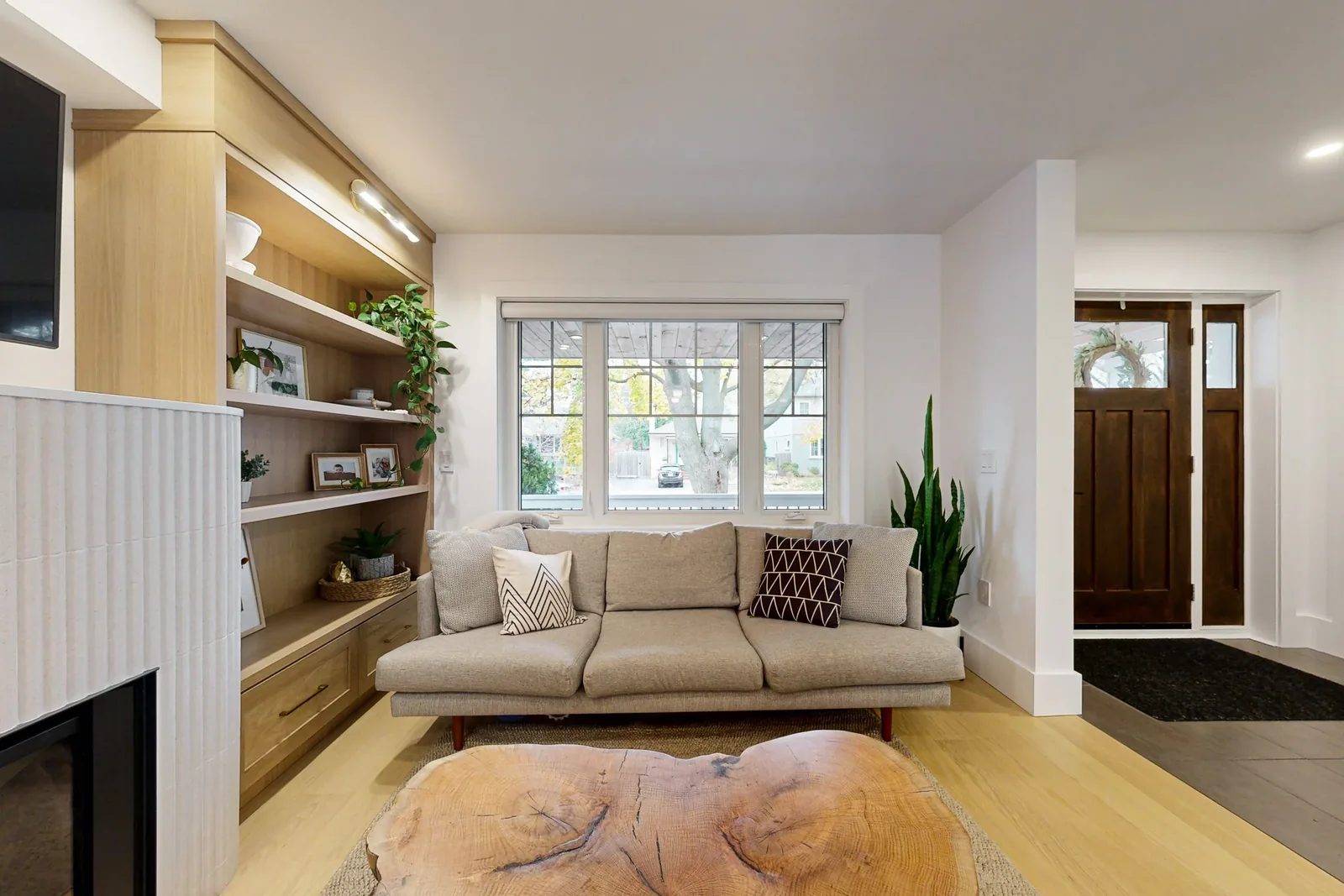Warm white living room with oak built ins, a front window, and a staged sofa beside the entry.