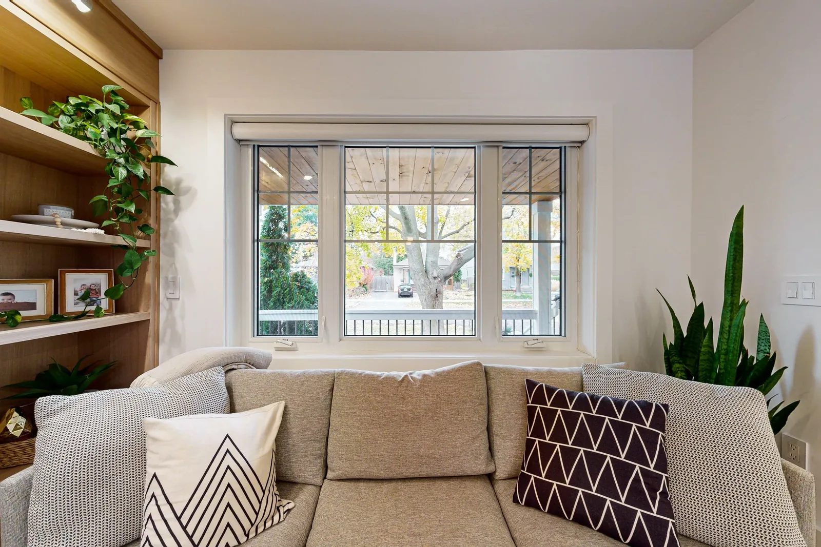 Bright living room with a beige sofa, oak shelving and a large gridded window overlooking the street.