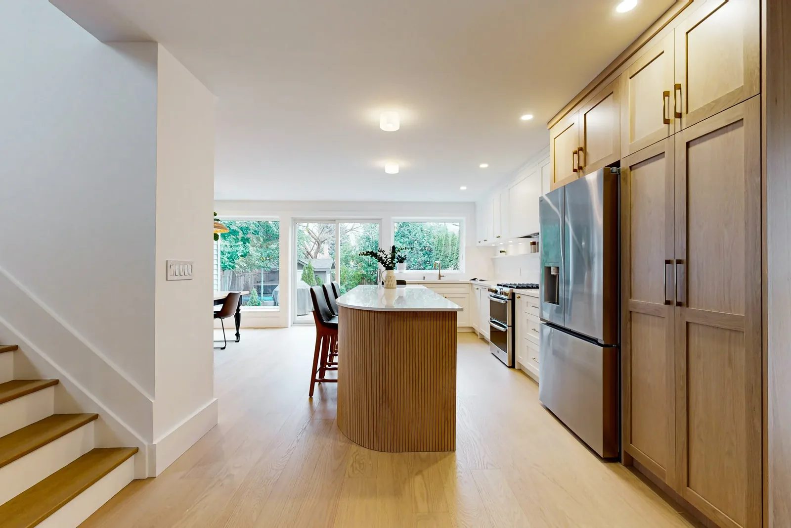 Bright open kitchen with white cabinetry, oak accents, a fluted island, and backyard-facing windows.