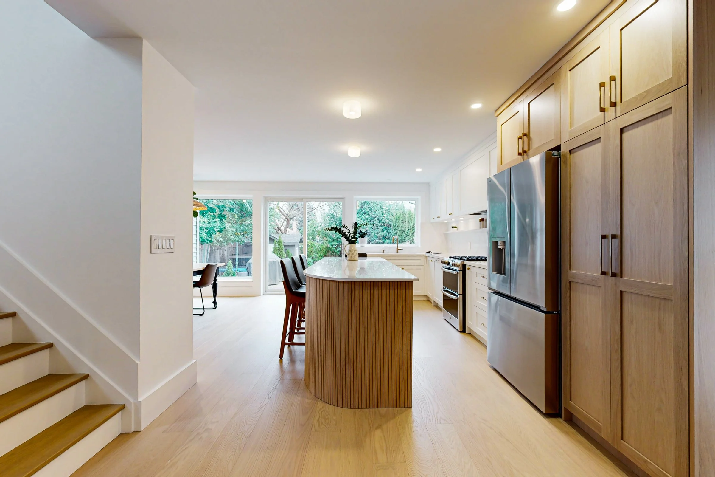 Bright open kitchen with white cabinetry, oak accents, a fluted island, and backyard-facing windows.