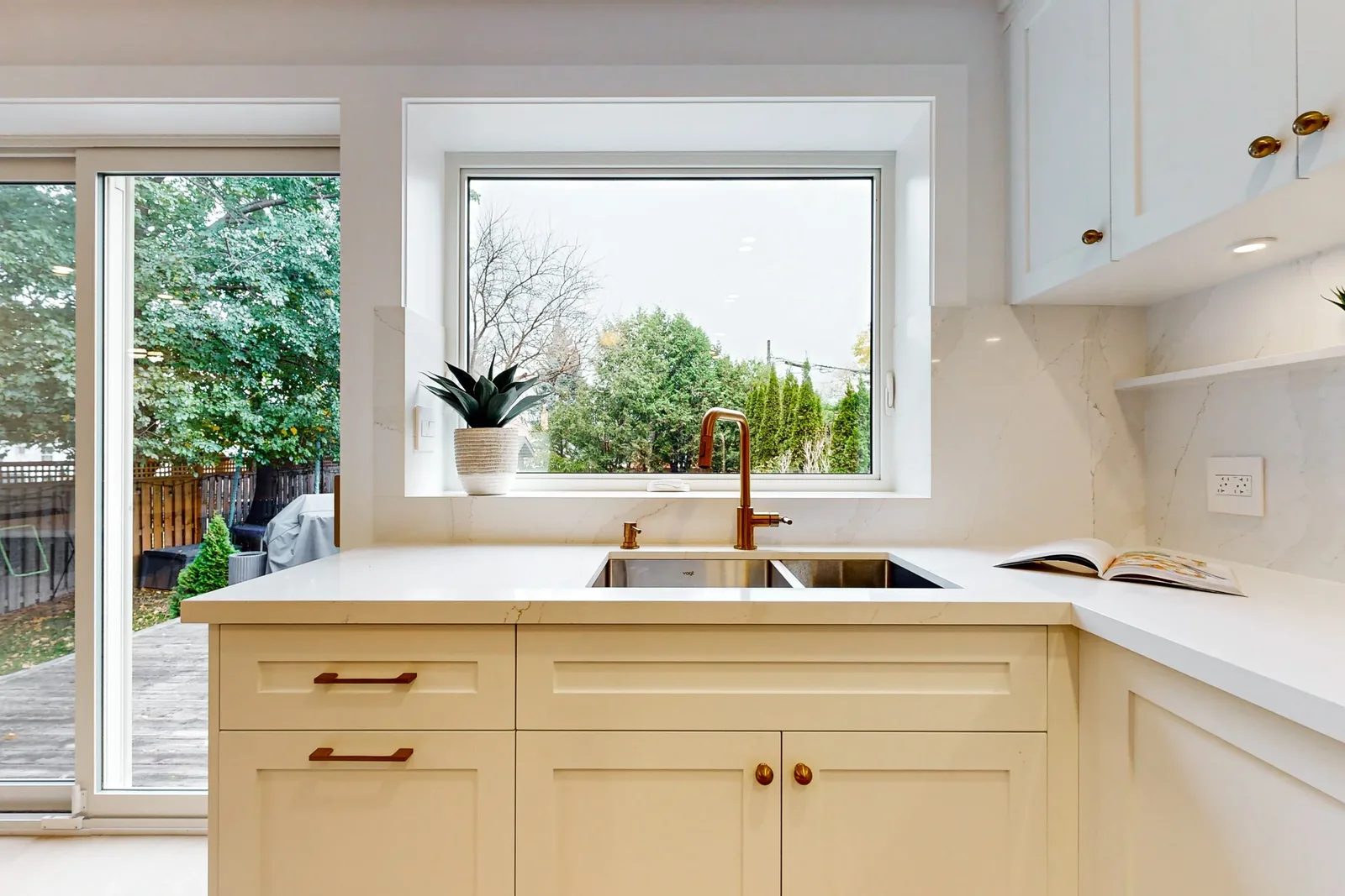 Bright white kitchen corner with quartz counters, brass tap, and a backyard-facing window.