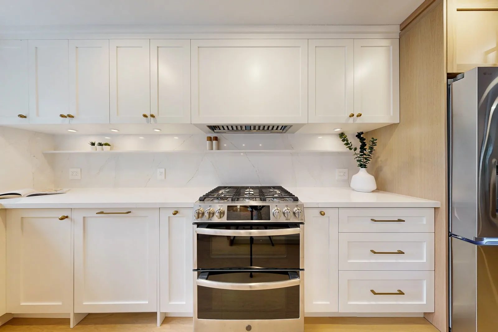 Warm white kitchen renovation with quartz surfaces, brass pulls, and a centred stainless gas range.