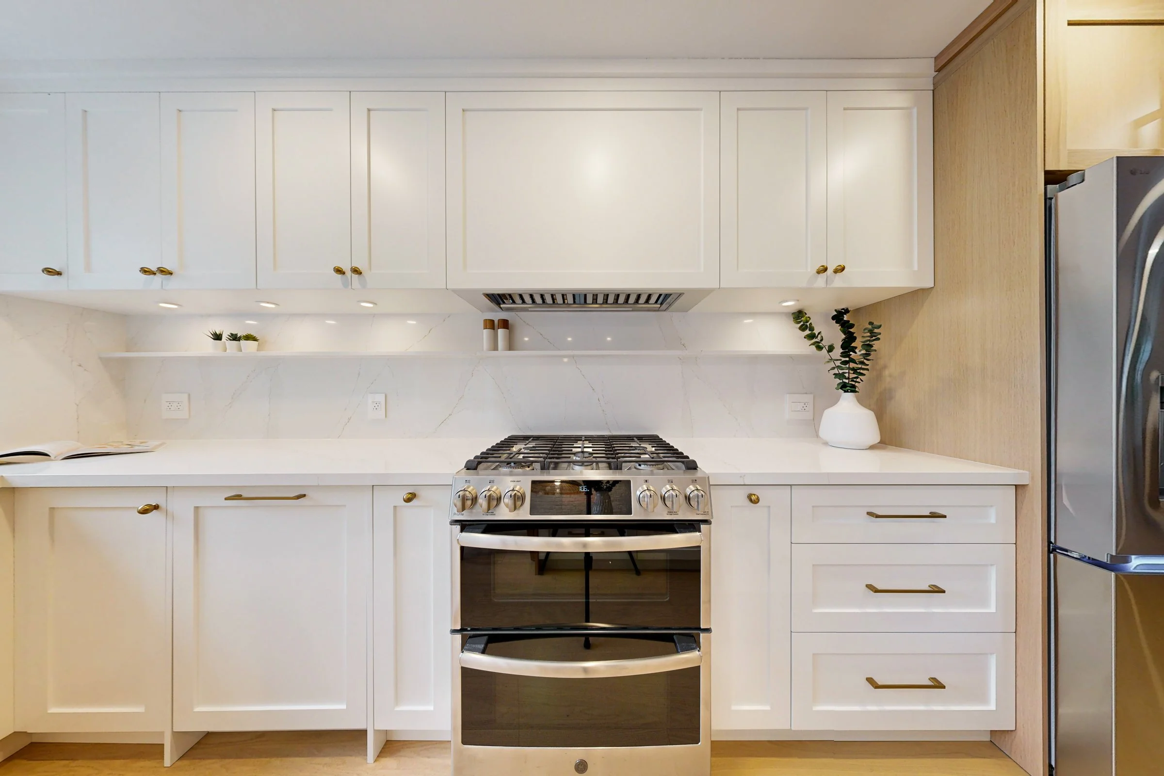 Warm white kitchen renovation with quartz surfaces, brass pulls, and a centred stainless gas range.